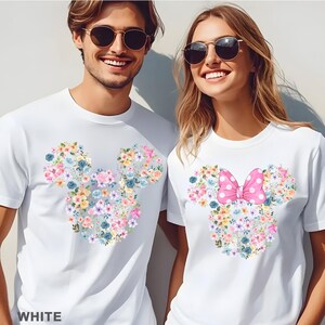 May include: White t-shirts with floral Mickey Mouse and Minnie Mouse designs. The Mickey Mouse design features a floral arrangement in pastel colors. The Minnie Mouse design includes a pink bow with white polka dots. The word "WHITE" is printed at the bottom.