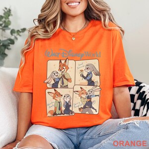 K&ouml;nnte beinhalten: Leuchtend orangefarbenes T-Shirt mit einer Grafik mit vier Panels von Zootopia-Charakteren. Auf dem oberen Panel steht "Walt Disney World" in blauer Schrift. Jedes Panel zeigt Nick Wilde und Judy Hopps in verschiedenen Posen. Das Wort "Orange" ist unten aufgedruckt.