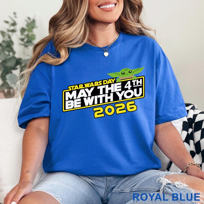 May include: Royal blue t-shirt with a graphic featuring the text "STAR WARS DAY MAY THE 4TH BE WITH YOU 2026" and a green cartoon character. The shirt is a solid color and has short sleeves.