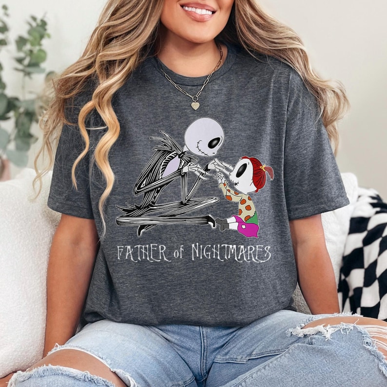 Puede incluir: Camiseta gris oscuro con un dise&ntilde;o de Jack Skellington y un ni&ntilde;o de Pesadilla antes de Navidad. El texto "FATHER OF NIGHTMARES" est&aacute; impreso en blanco. La camiseta es de estilo casual.