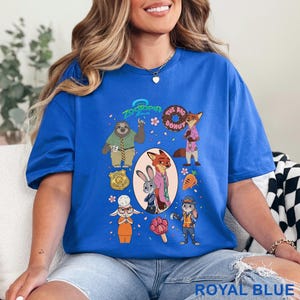 K&ouml;nnte beinhalten: Ein k&ouml;nigsblaues T-Shirt mit einem Zootopia-Grafikdruck, der Charaktere wie Flash, Nick Wilde, Judy Hopps und Bellwether zeigt. Das Design enth&auml;lt den Text Zootopia und The Big Donut sowie Symbole wie ein Abzeichen, eine Karotte und ein pfotenf&ouml;rmiges Eis.
