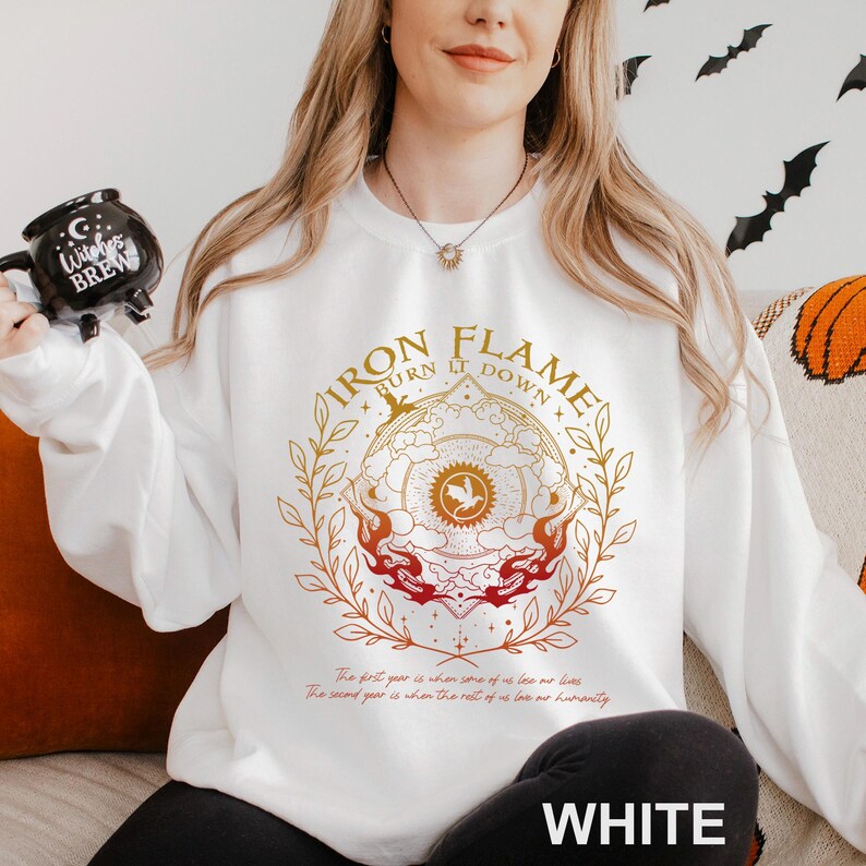 May include: White sweatshirt with a circular graphic that reads "IRON FLAME BURN IT DOWN" in gold and red. The design includes a bird emblem and floral elements. Below the graphic is text. The word "WHITE" is printed at the bottom.