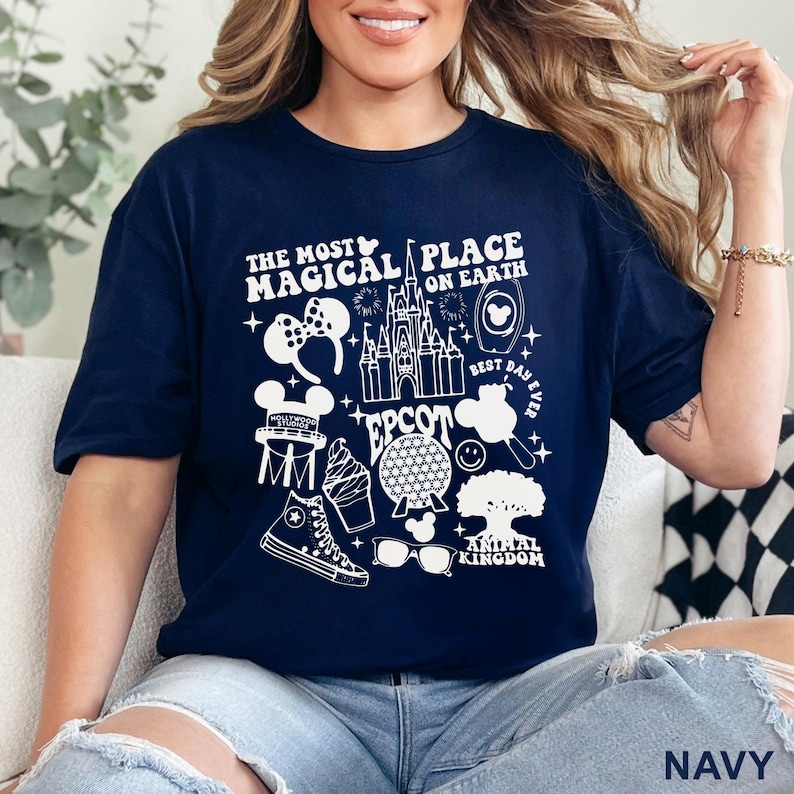 May include: Navy blue t-shirt with a white graphic design featuring the text "THE MOST MAGICAL PLACE ON EARTH" and various Disney-themed icons, including a castle, Mickey Mouse ears, and a sneaker. The word "EPCOT" and "ANIMAL KINGDOM" are also visible.