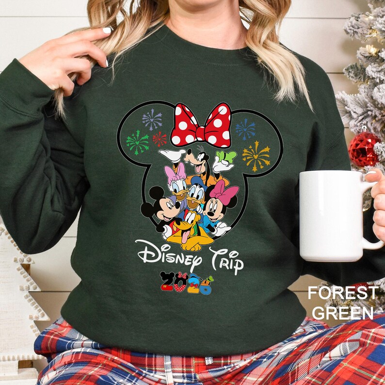 May include: Forest green sweatshirt featuring a Disney Trip design. The design includes Mickey and Minnie Mouse, Donald and Daisy Duck, Goofy, and Pluto. The design is in the shape of Mickey Mouse's head with a red polka dot bow. The text "Disney Trip" is below the characters.