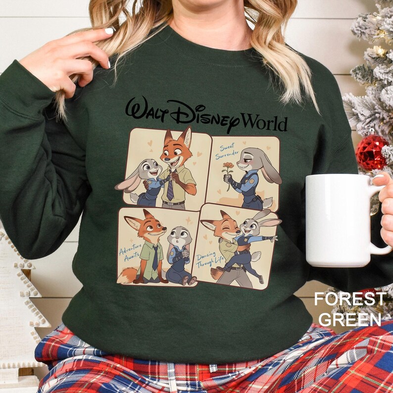 May include: Forest green sweatshirt featuring a four-panel graphic of Nick Wilde and Judy Hopps from Zootopia. The top panel reads "Walt Disney World" and the bottom right panel reads "Dancing Through Life". A white mug is held in the hand.