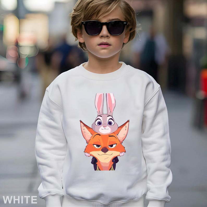 May include: White sweatshirt featuring a graphic of Judy Hopps and Nick Wilde from Zootopia. The design shows Judy Hopps, a gray rabbit, atop Nick Wilde, an orange fox. The word "WHITE" is printed at the bottom of the sweatshirt.