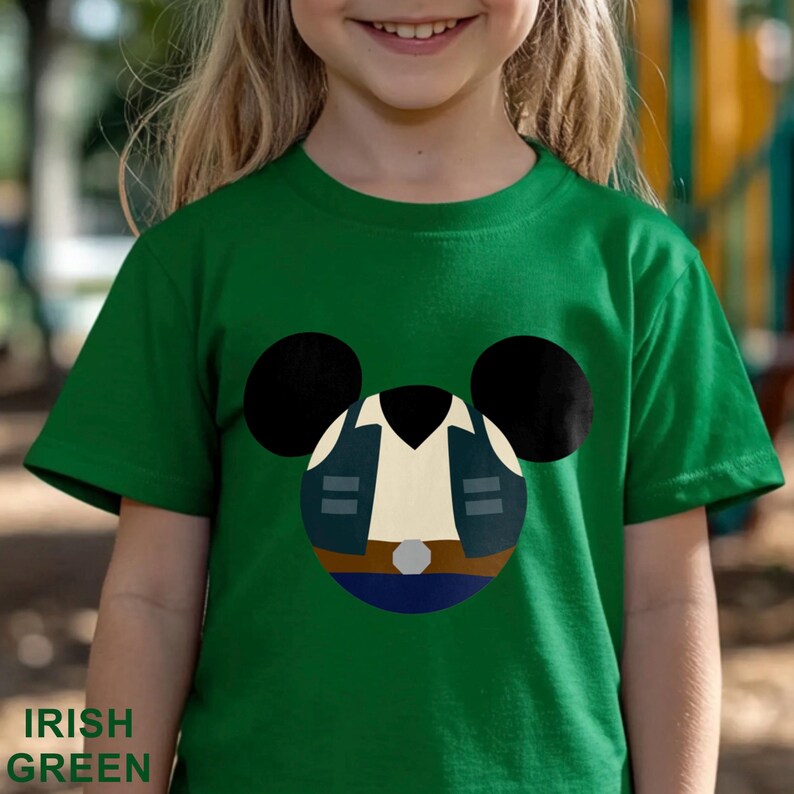 May include: Irish green t-shirt featuring a cartoon design of a character's outfit within a Mickey Mouse head shape. The design includes a navy blue jacket, a tan shirt, and a blue belt. The text "IRISH GREEN" is at the bottom.