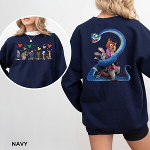 May include: A navy blue sweatshirt featuring a graphic on the back of a large blue snake coiled around a fox and a rabbit character. The front chest area displays a smaller horizontal row of various animated characters with colorful mouse-ear icons.