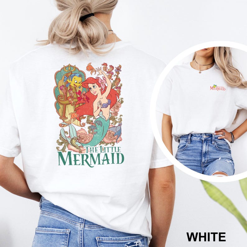 May include: White t-shirt featuring a colorful graphic of Ariel from The Little Mermaid, with the text "The Little Mermaid" in green. The shirt also has a small "Mermaid" text on the front.