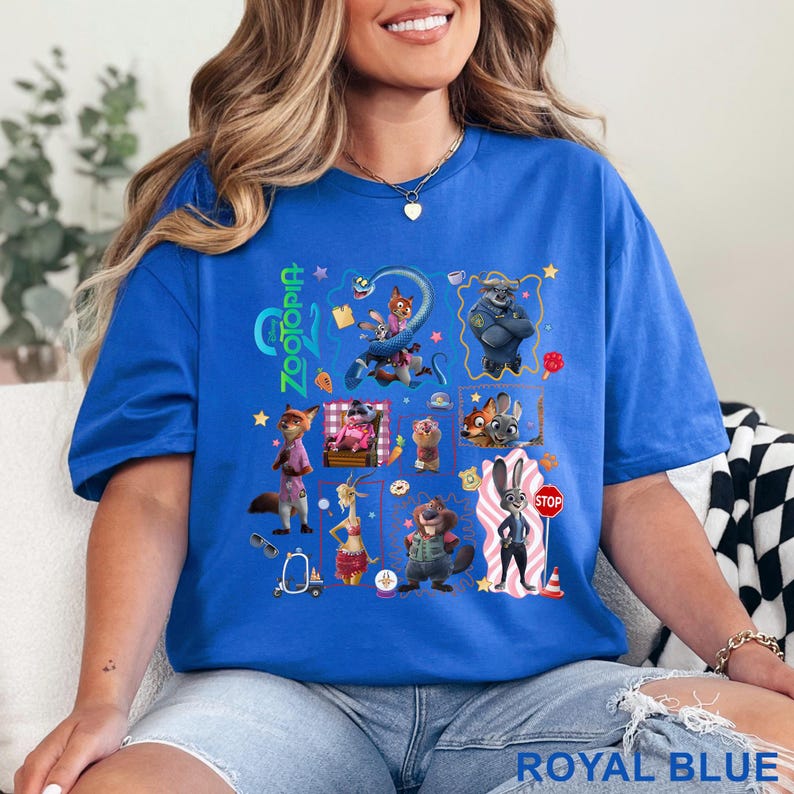 May include: Royal blue t-shirt featuring a colorful graphic of characters from the animated movie Zootopia. The word "Zootopia" is printed in green on the left side. The shirt is made of a soft material.