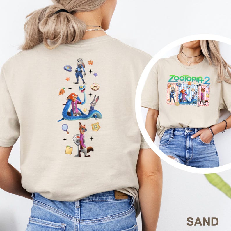 May include: A sand-coloured t-shirt with a colourful graphic of characters from Zootopia 2. The back of the shirt displays a vertical arrangement of Zootopia characters and icons. The front of the shirt has the text "Zootopia 2" in green and blue.