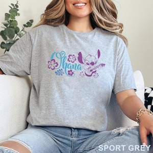 Op de afbeelding: Een sportgrijs t-shirt met een grafische print van het personage Stitch die ukelele speelt naast het woord Ohana in blauw schrift, omringd door paarse hibiscusbloemen en tropische bladeren, met de tekst SPORT GREY in de onderste hoek.