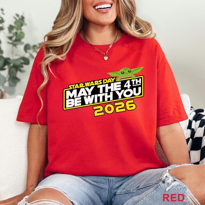 May include: A red t-shirt featuring the text "STAR WARS DAY MAY THE 4TH BE WITH YOU 2026" in white and yellow, with a green cartoon character. The shirt is a vibrant red color.