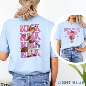 May include: Light blue t-shirt featuring a cartoon fox character in a pink shirt and sunglasses. The back of the shirt has the text "NICK" repeated vertically with the character's image. The front of the shirt has the text "NICK WIDE" with the character's image.