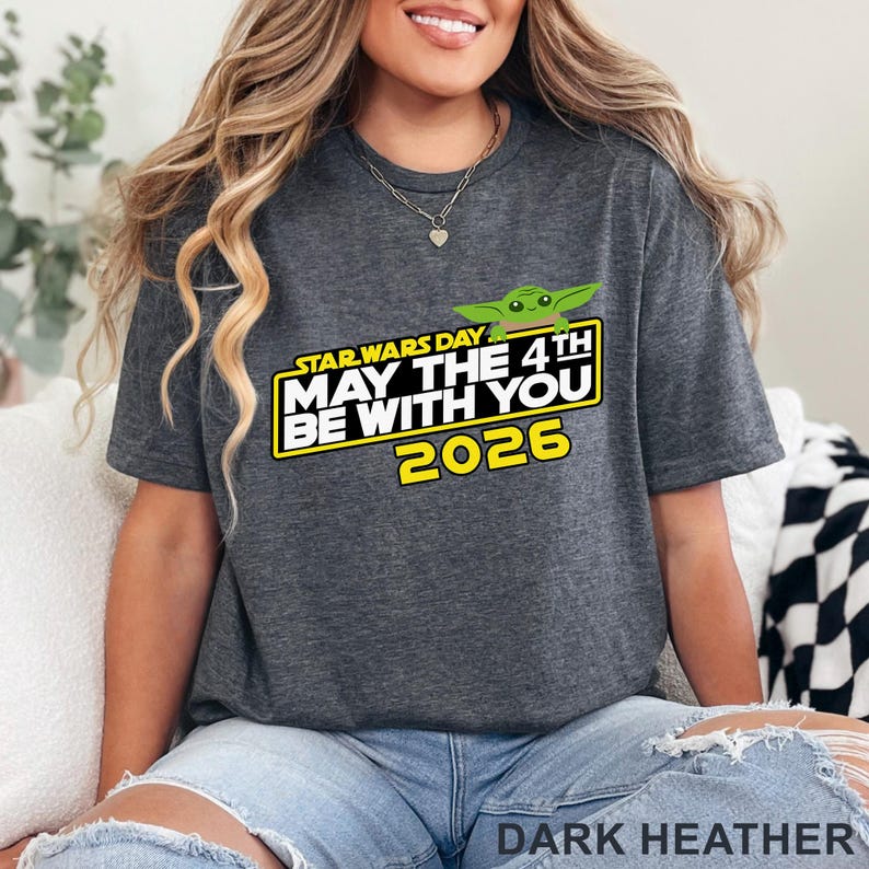 May include: Dark heather gray t-shirt featuring the text "Star Wars Day May the 4th Be With You 2026" in white and yellow, with a green cartoon character. The shirt is a comfortable, casual style.