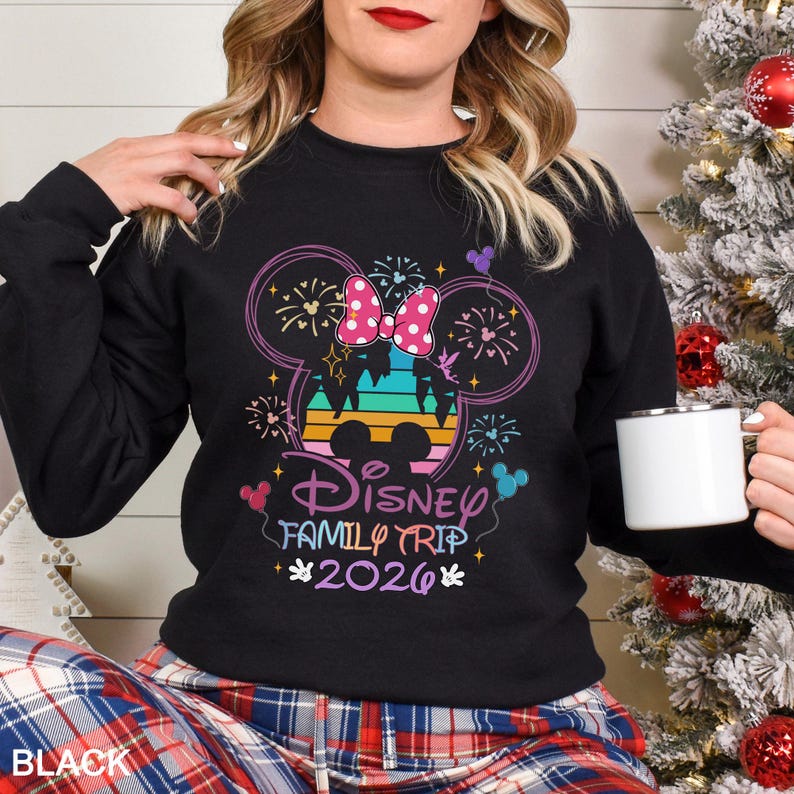 May include: Black sweatshirt with a colorful Disney Family Trip 2026 graphic. The design features a Minnie Mouse bow, fireworks, and a castle silhouette. The text "Disney Family Trip 2026" is in a playful font.
