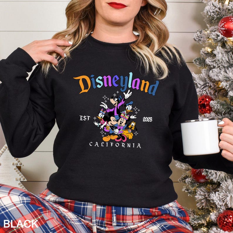 Puede incluir: Sudadera negra de Disneyland con el logotipo multicolor de Disneyland y un gr&aacute;fico de Mickey Mouse, Minnie Mouse, Donald Duck y Goofy. El texto "EST 2025 CALIFORNIA" tambi&eacute;n est&aacute; impreso en la sudadera.