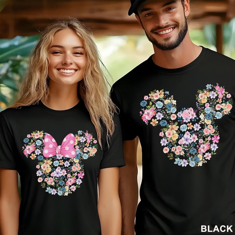 May include: Black t-shirts featuring a floral Mickey Mouse design. One shirt has a pink polka dot bow. The floral design includes pink, blue, yellow, and purple flowers. The word "BLACK" is printed in white.