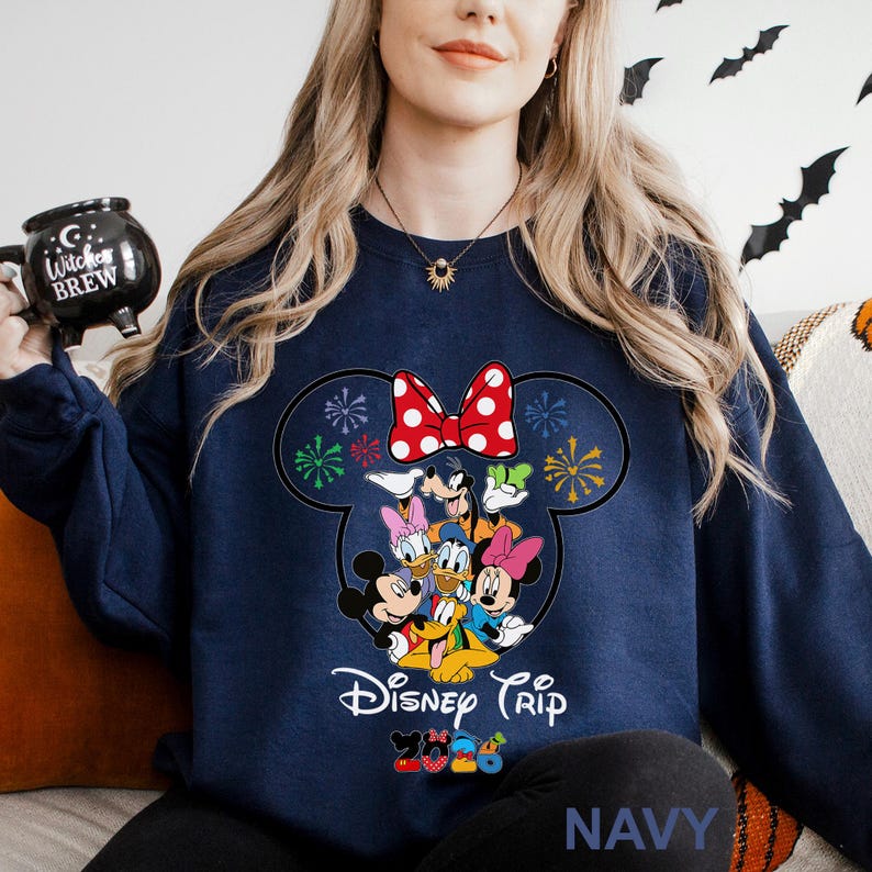 May include: Navy blue sweatshirt featuring a Mickey Mouse silhouette with a red polka dot bow and Disney characters. The words "Disney Trip" are printed below the characters. The word "NAVY" is printed at the bottom.