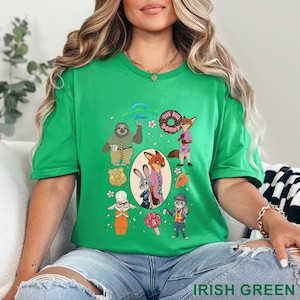 K&ouml;nnte beinhalten: Ein hellgr&uuml;nes Kurzarm-T-Shirt mit einem Zootopia-Grafikdruck. Das Design zeigt Charaktere wie Judy Hopps und Nick Wilde, eine Polizeimarke, einen Donut, eine Karotte und ein pfotenf&ouml;rmiges Eis am Stiel, die in einer Collage angeordnet sind.