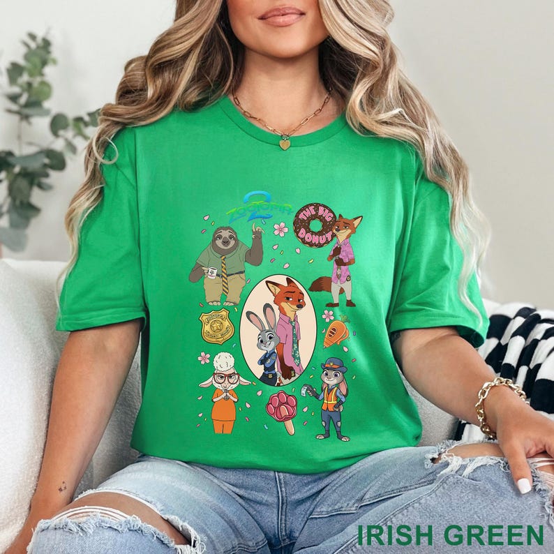 K&ouml;nnte beinhalten: Ein hellgr&uuml;nes Kurzarm-T-Shirt mit einem Zootopia-Grafikdruck. Das Design zeigt Charaktere wie Judy Hopps und Nick Wilde, eine Polizeimarke, einen Donut, eine Karotte und ein pfotenf&ouml;rmiges Eis am Stiel, die in einer Collage angeordnet sind.
