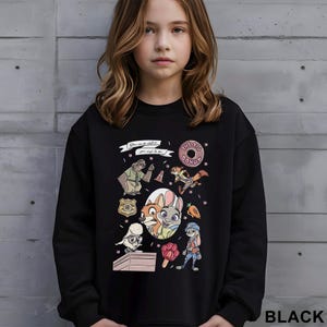 May include: Black sweatshirt featuring colorful cartoon characters and the text "THE BIG DONUT." The design includes a donut, a sloth, a fox, a rabbit, and other characters. The text "You can be whatever you wish to be" is also present.