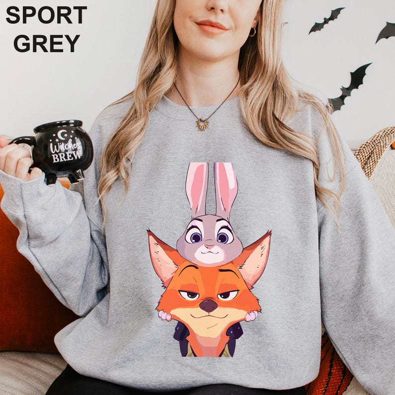 May include: Sport grey sweatshirt featuring a cartoon image of a fox and a bunny. The fox has orange fur and a sly expression, while the bunny has gray fur and large ears. The sweatshirt is a light gray color.