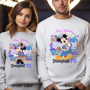 May include: Sport grey and white sweatshirts featuring Mickey and Minnie Mouse with the text "Walt Disney Disneyland 70". The sweatshirts have colorful graphics of amusement park attractions.
