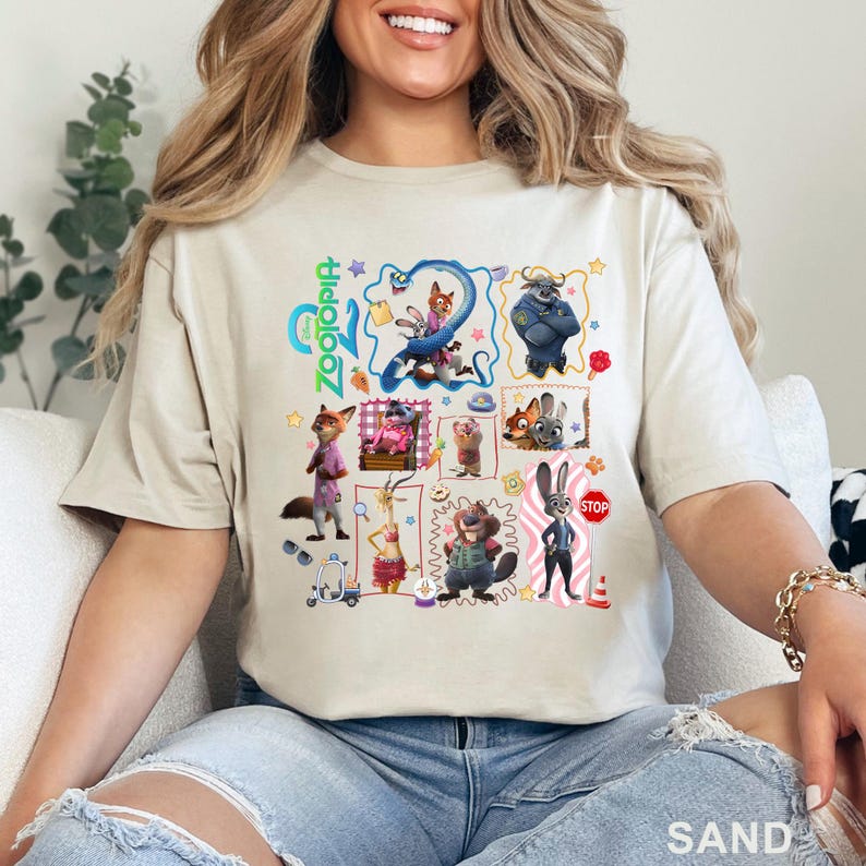 May include: Sand-colored t-shirt featuring a colorful graphic of characters from the animated movie "Zootopia." The design includes various animal characters in a grid layout, with the movie's title in green and blue. The shirt is made of a soft material.