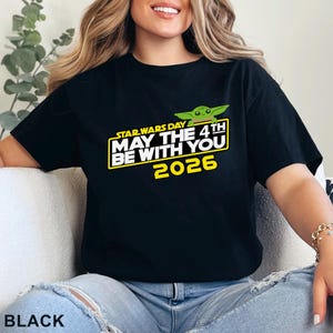 May include: Black t-shirt featuring a Star Wars Day design with the text "May the 4th Be With You 2026" in yellow and white, along with a green cartoon character. The shirt is a classic crew neck.
