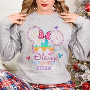 May include: Sport Grey sweatshirt featuring a Disney Family Trip 2026 design. The design includes a castle, a pink polka dot bow, and fireworks within a Mickey Mouse head outline. The text "Disney Family Trip 2026" is in a colorful font.