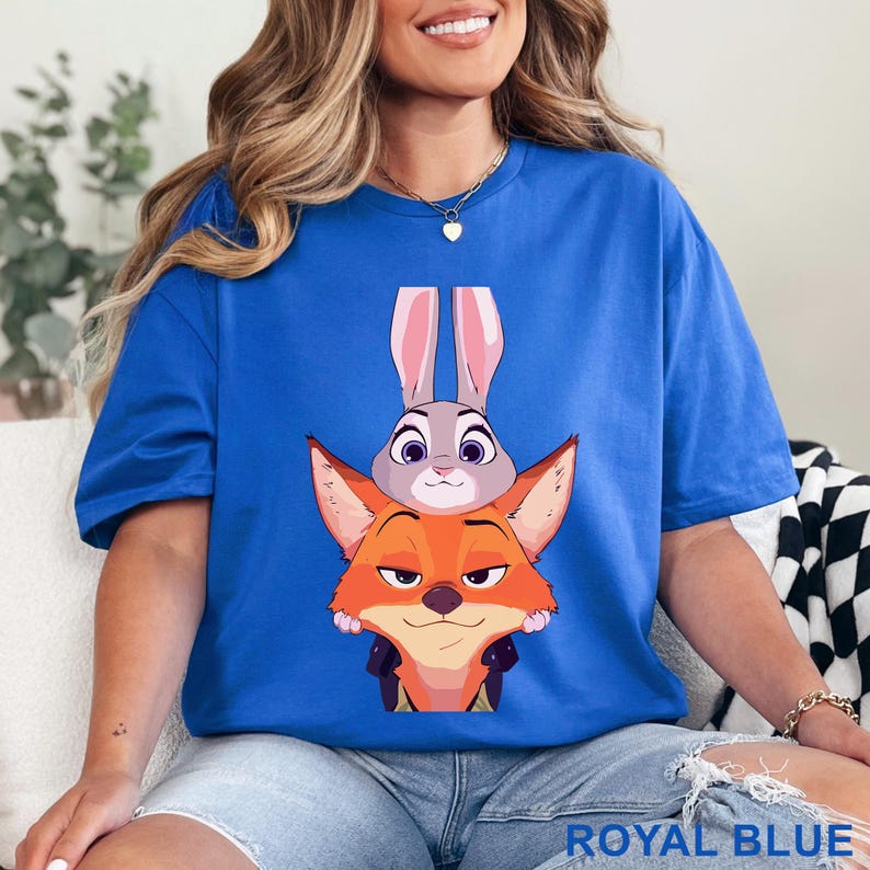 May include: Royal blue t-shirt featuring a cartoon illustration of Judy Hopps the rabbit and Nick Wilde the fox from Zootopia. The text "ROYAL BLUE" is printed at the bottom of the shirt.