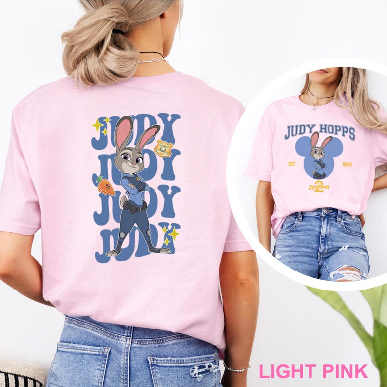 May include: Light pink t-shirts featuring Judy Hopps from Zootopia. One shirt has a large graphic on the back with Judy in a police uniform and the text "Judy". The other shirt has a smaller design on the front with the text "Judy Hopps".