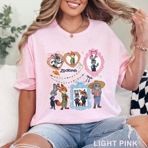 Puede incluir: Una camiseta rosa claro con un estampado gr&aacute;fico de Zootopia que muestra a los personajes Judy Hopps y Nick Wilde. El dise&ntilde;o incluye marcos con forma de coraz&oacute;n y rectangulares, un icono de zanahoria y el texto Welcome to Zootopia.