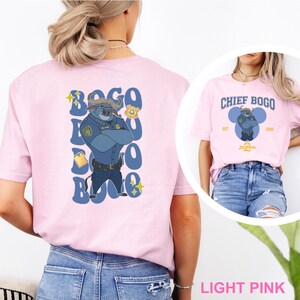 May include: Light pink t-shirts featuring Chief Bogo from Zootopia. One shirt has a large graphic on the back with the text "Bogo" and an illustration of Chief Bogo. The other shirt has "Chief Bogo" printed on the front.