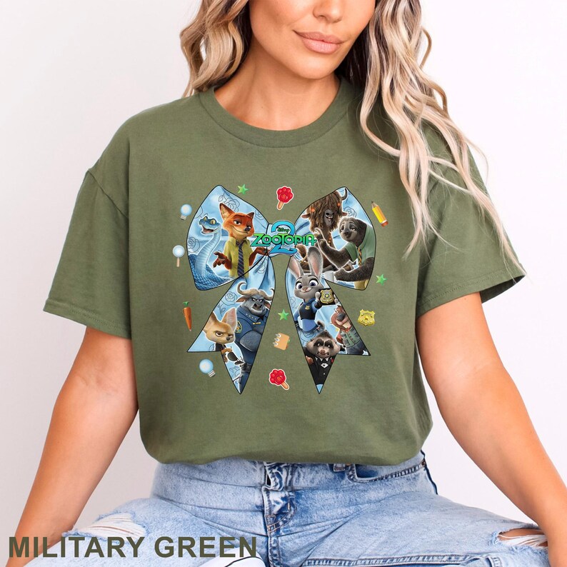 Op de afbeelding: Militairgroen T-shirt met een groot strikdesign met personages uit de film Zootopia. De strik is lichtblauw en bevat verschillende personages en het woord "Zootopia". Het shirt is effen van kleur.