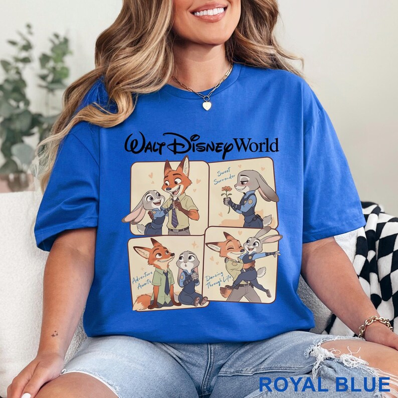 May include: Royal blue t-shirt featuring a Walt Disney World graphic. The graphic includes four panels with cartoon images of a fox and a rabbit. Text on the shirt includes "Walt Disney World", "Sweet Surrender", "Adventure Awaits", and "Dancing Through Life".