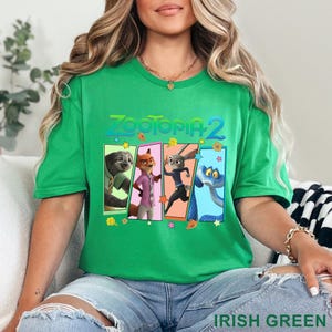 May include: Green t-shirt with the text "ZOOTOPIA 2" and a graphic of characters from the film. The graphic includes a sloth, fox, rabbit, and snake. The shirt is made of a soft material.