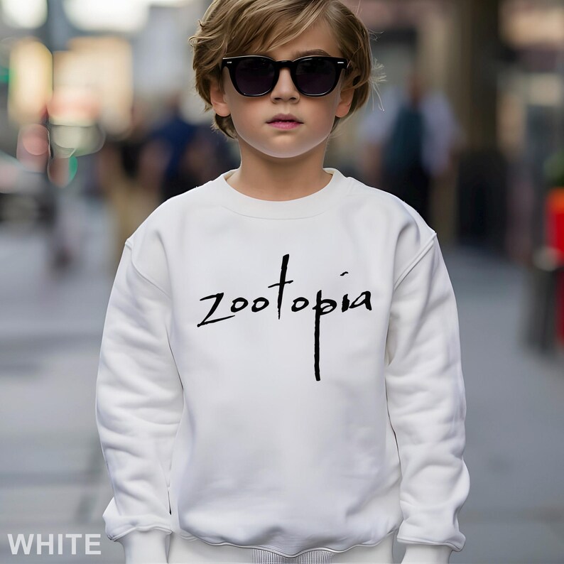 May include: A white sweatshirt with the word "Zootopia" in black script. The sweatshirt is long-sleeved and has a crew neck. The image also shows a person wearing black sunglasses.