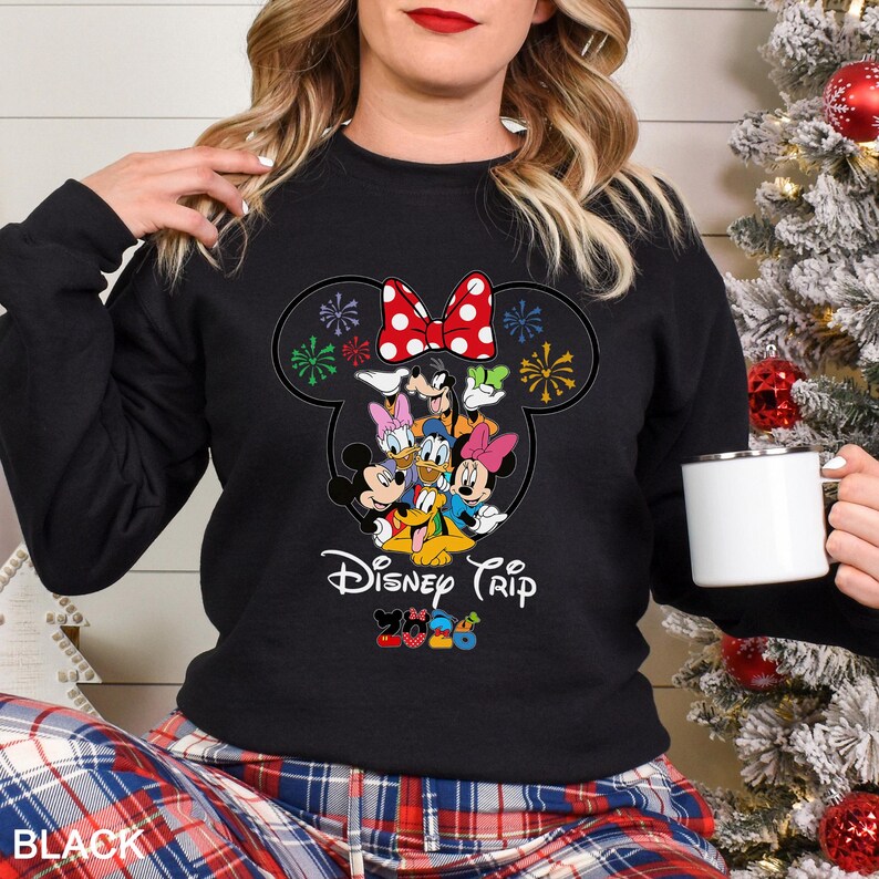 May include: Black sweatshirt featuring a Disney Trip design with Mickey Mouse, Minnie Mouse, Donald Duck, and other characters. The design includes a red bow and colorful fireworks. The word "BLACK" is printed at the bottom.