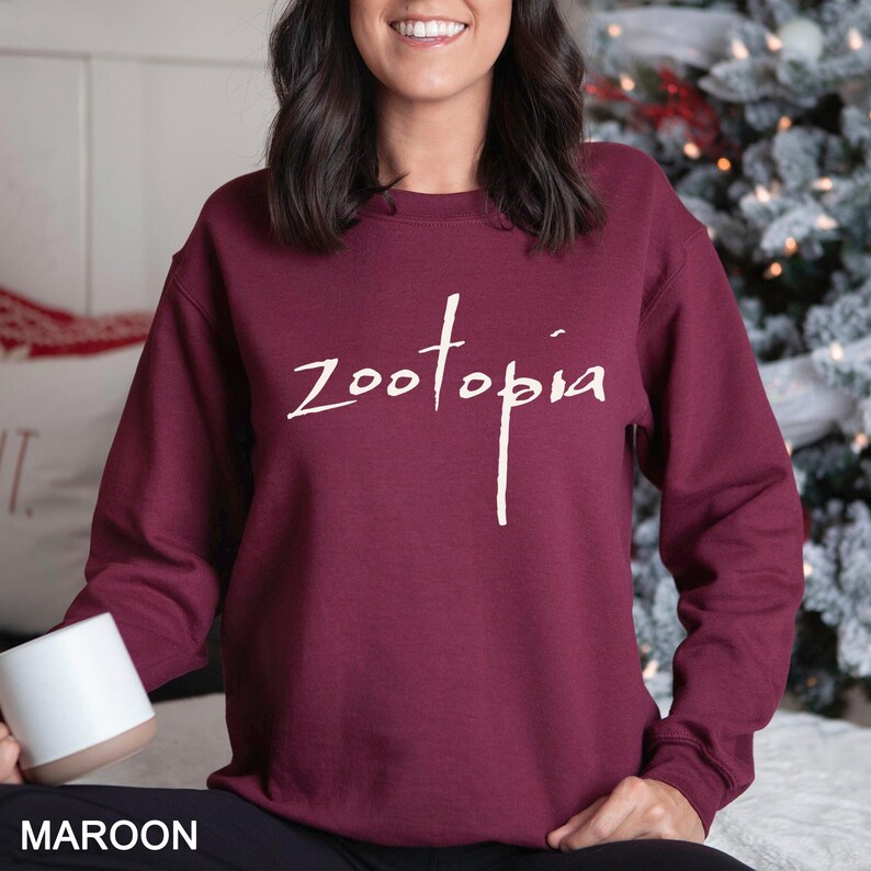 May include: Maroon sweatshirt with the word "Zootopia" in white script. The sweatshirt is a solid color and has a crew neck. The word "MAROON" is printed in white at the bottom of the image.