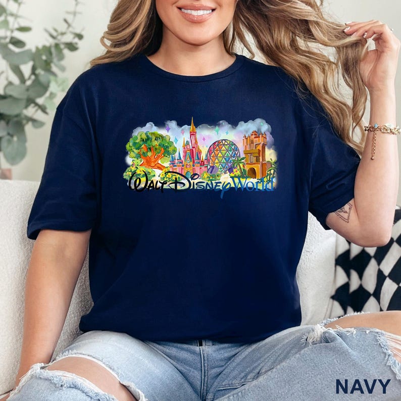 May include: A navy blue short-sleeve t-shirt featuring a colorful graphic print of the Walt Disney World theme park landmarks, including the castle, the geodesic sphere, and the tree of life, with the text Walt Disney World printed below.