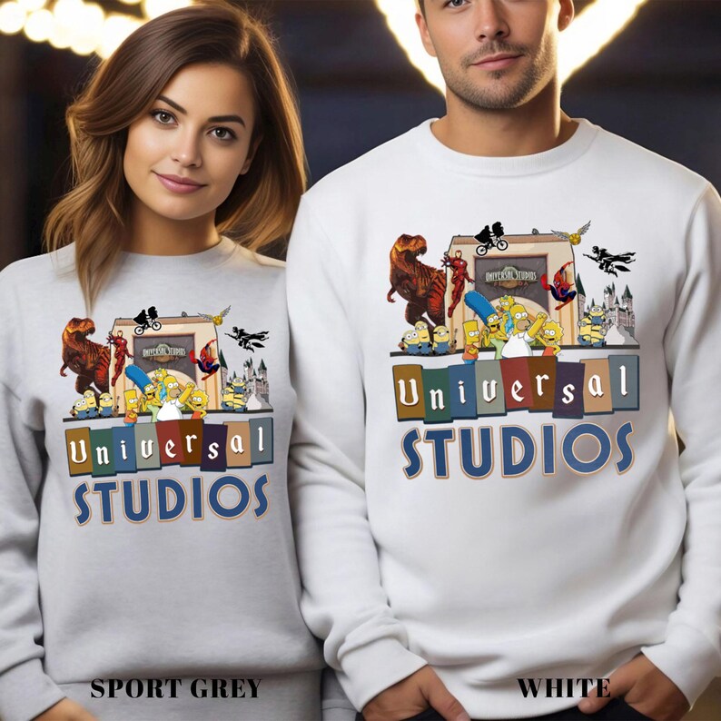 May include: Sport grey and white sweatshirts featuring a colorful graphic design with the text "Universal Studios". The design includes cartoon characters, dinosaurs, and the Universal Studios logo. The sweatshirts are long-sleeved.