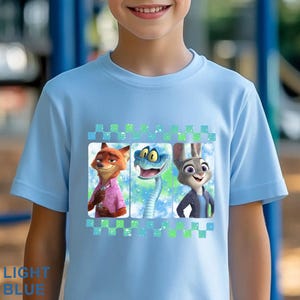 May include: Light blue t-shirt featuring three cartoon characters: a fox in a pink shirt, a snake, and a rabbit in a blue jacket. The design is framed with a checkered pattern. The words "LIGHT BLUE" are printed at the bottom of the shirt.