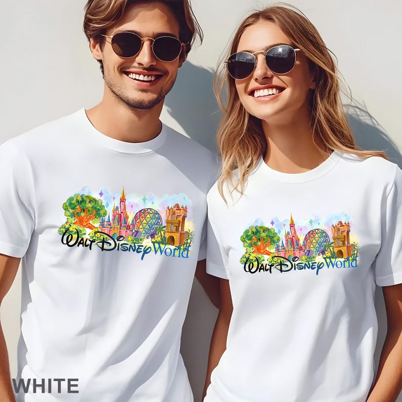 May include: Two white short-sleeved t-shirts featuring a colorful graphic print of the Walt Disney World theme park landmarks, including a castle, a geodesic sphere, and a tower, with the text Walt Disney World in a stylized blue script font.