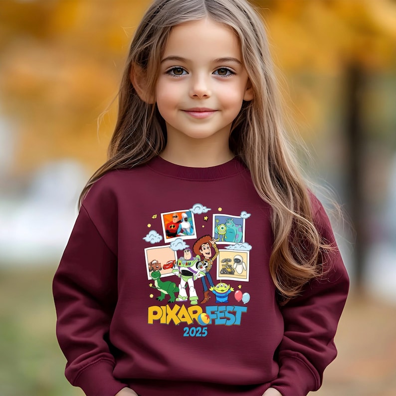 Może przedstawiać: Bordowa bluza z kolorową grafiką postaci z film&oacute;w Pixar i napisem "PIXAR FEST 2025". Projekt zawiera obrazy postaci z r&oacute;żnych film&oacute;w Pixara. Bluza jest noszona przez młodą dziewczynę.
