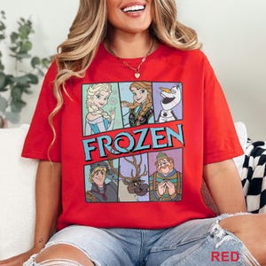 May include: A red t-shirt featuring a graphic design with characters from the animated movie "Frozen." The design includes Elsa, Anna, Olaf, Kristoff, and Sven, with the word "FROZEN" in large, blue letters. The shirt is a vibrant red color.