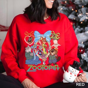 May include: A red sweatshirt with a vibrant graphic of characters from the animated film "Zootopia." The design includes Judy Hopps, Nick Wilde, and other characters, framed by a blue bow and decorative elements. The word "Zootopia" is written in green.