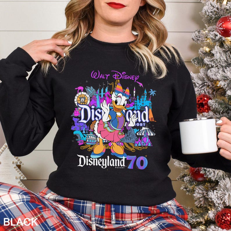 May include: Black sweatshirt featuring a colorful graphic of Daisy Duck in front of Disneyland Resort imagery. The design includes the text "Walt Disney", "Disneyland Resort", and "70". The sweatshirt is a crew neck style.
