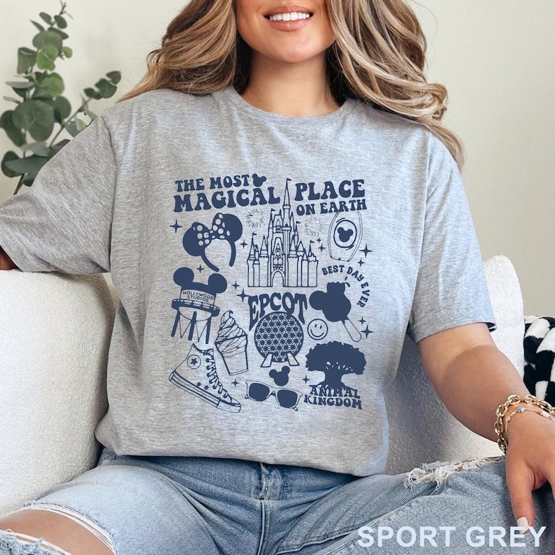 May include: Sport grey t-shirt with a navy blue graphic featuring the text "THE MOST MAGICAL PLACE ON EARTH" and various Disney-themed icons, including a castle, Mickey Mouse ears, and a pair of sunglasses.